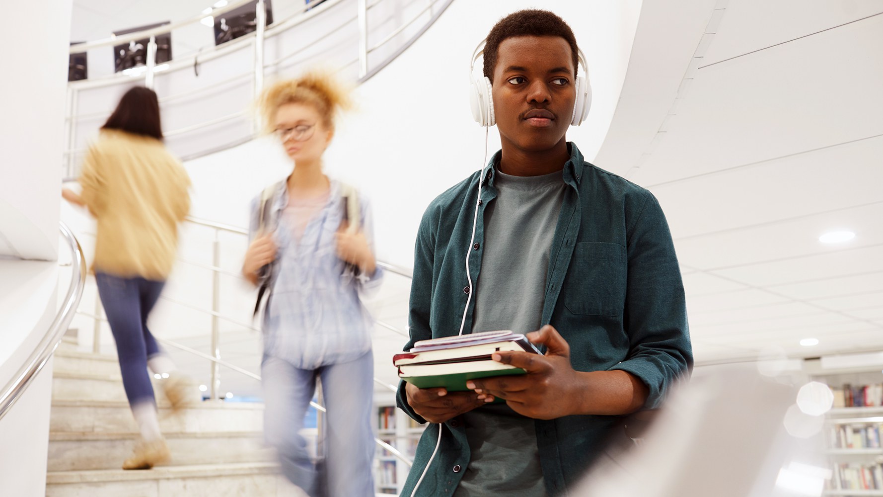 Ein junger Student steigt mit Büchern in den Händen in einer Bibliothek eine Treppe runter