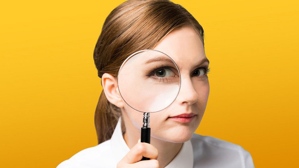 Une femme regarde à travers une loupe, son œil apparaît grossi.