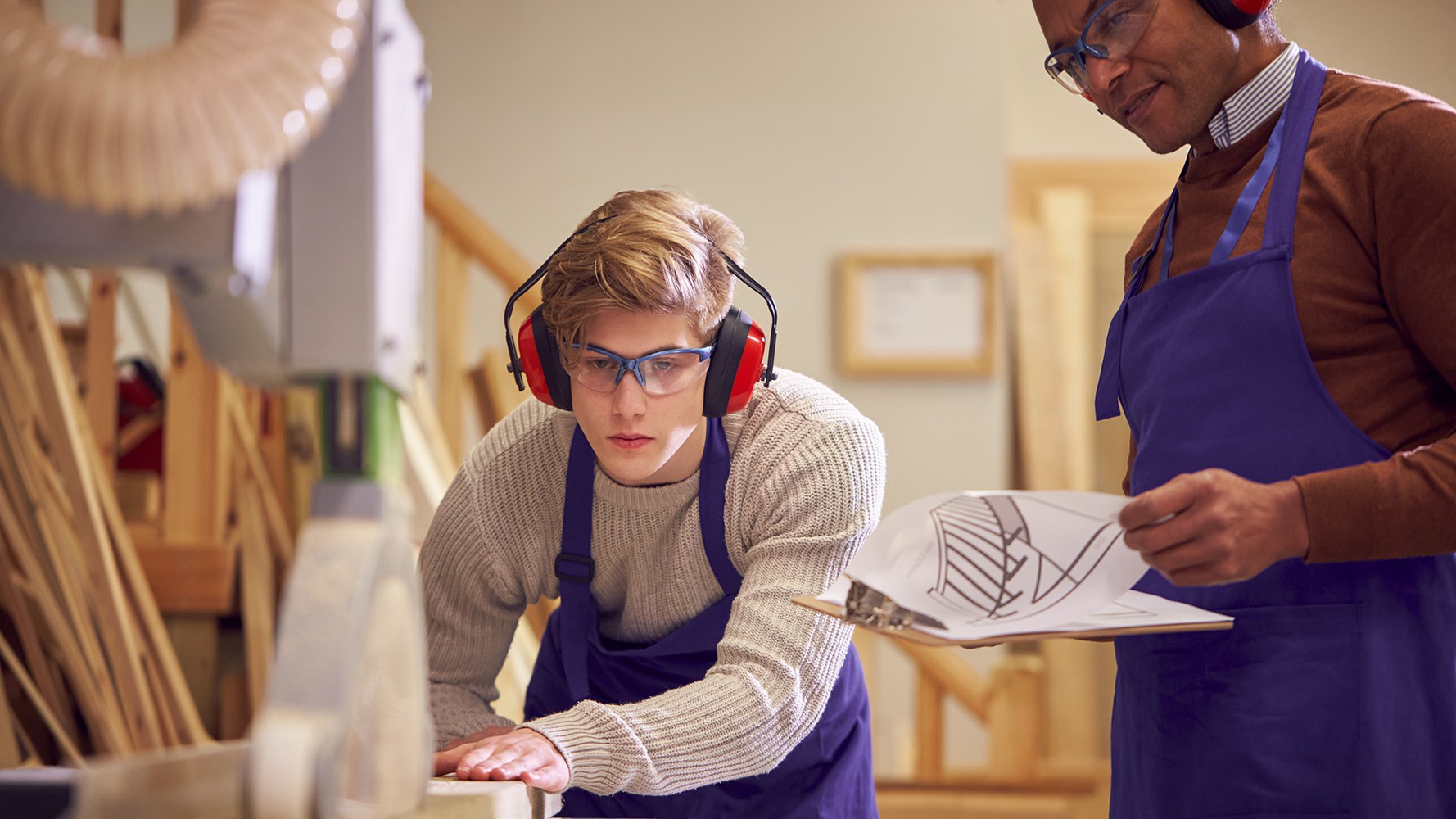 Un jeune menuisier travaille et est observé par son maître d'apprentissage