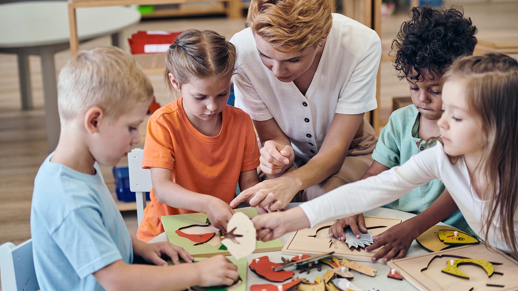 Quatre enfants et une enseignante sont assis autour d'une table et jouent à un jeu.