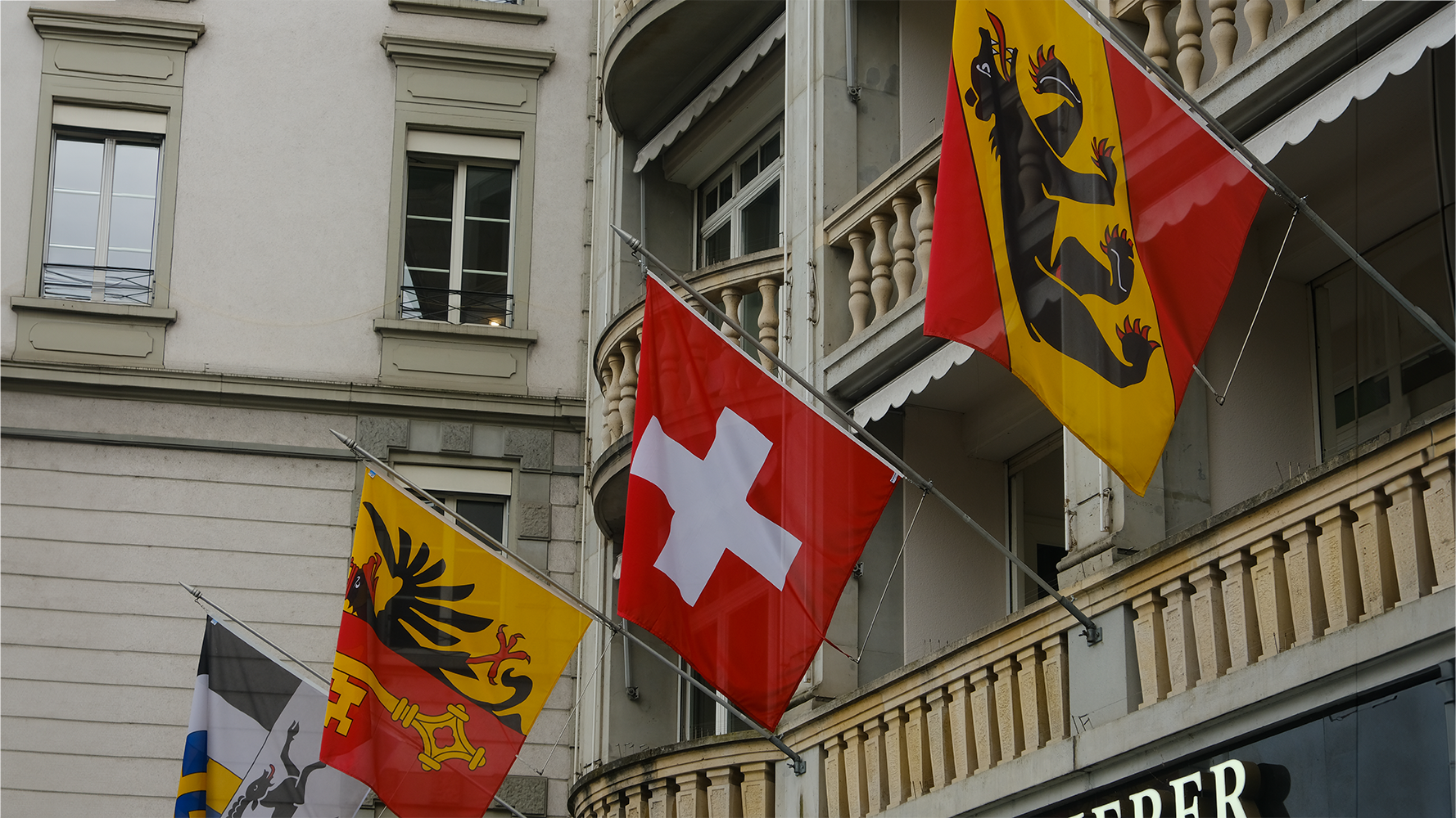 Flaggen der Kantone Graubünden, Genf und Bern sowie die Schweizerfahne an einer Häuserwand