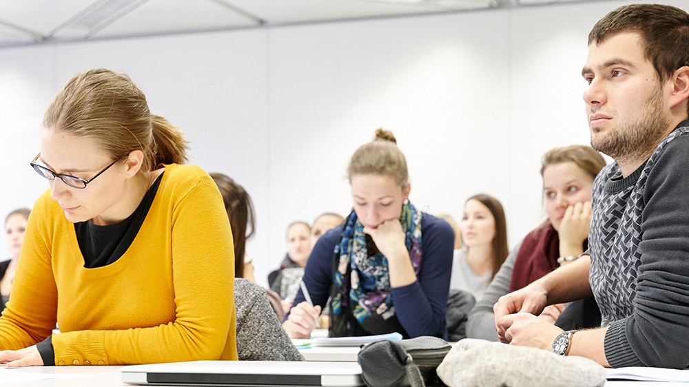 Les étudiants s'assoient à des tables, prennent des notes et écoutent avec attention