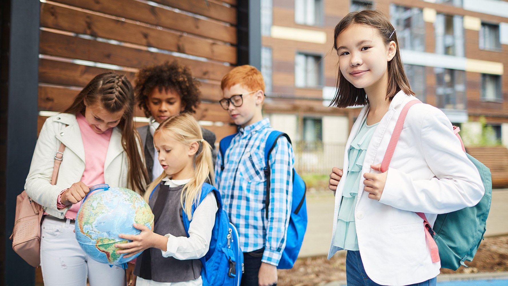 Quatre enfants regardent un globe terrestre, au premier plan se trouve une cinquième fille qui regarde la caméra.