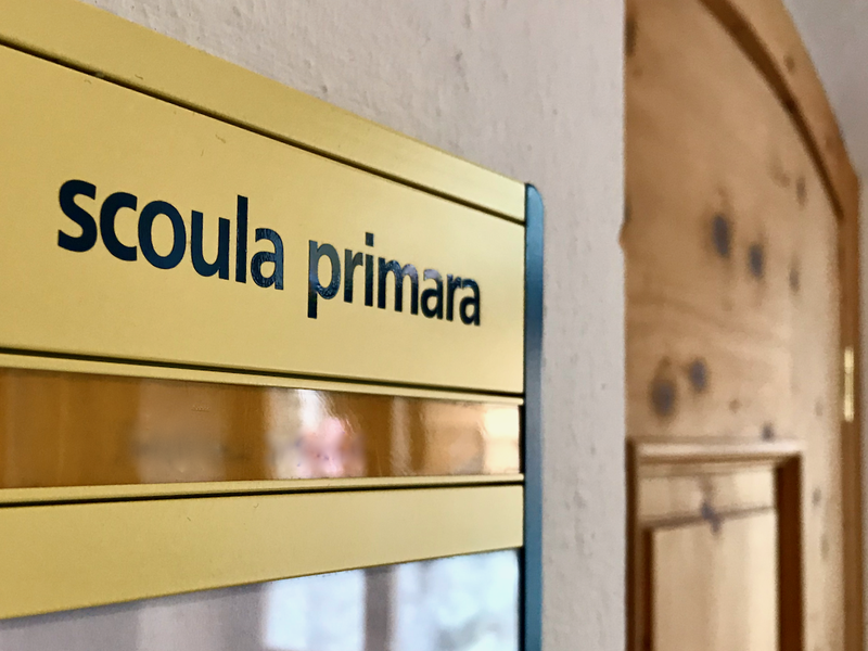 Une plaque de porte dans un bâtiment scolaire, sur laquelle figure l’inscription «scoula primara»